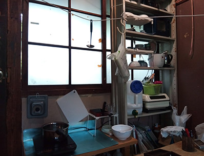 調理場の写真。左側の机の上にIHコンロがある。右側にはスチールラックがあり、食器類が置いてある。